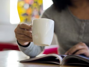 a girl is drinking coffee and reading a magazine.