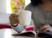 a girl is drinking coffee and reading a magazine.